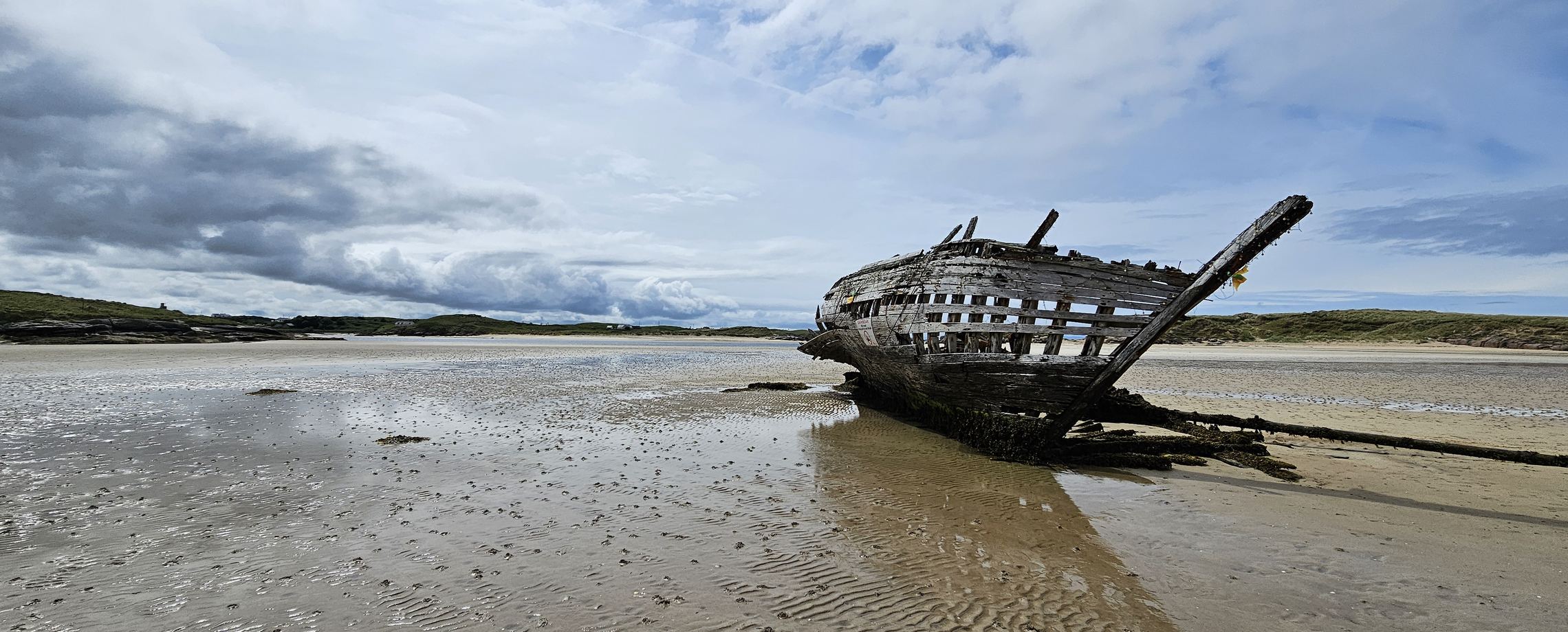 A weathered wooden shipwreck resting on a tidal beach.